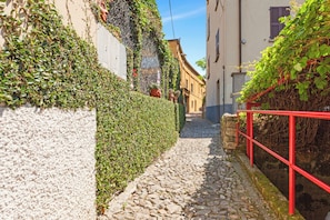 Un estrecho callejón adoquinado, con un muro de piedra a un lado y una barandilla metálica roja al otro.