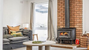 A cozy living room with a fireplace, a sofa, a table, and a view of the outdoors. - The Hide at Big Hill (Big Hill)