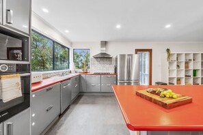 Een moderne keuken met roestvrijstalen apparatuur, een rode aanrecht en uitzicht op het groen.