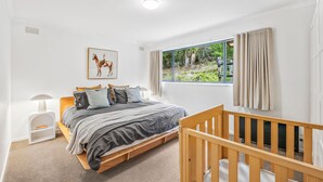 A bedroom with a bed, a crib, a window with curtains, a painting, and a lamp. - The Hide at Big Hill (Big Hill)