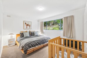 A bedroom with a bed, a crib, a window with curtains, a painting, and a lamp. - The Hide at Big Hill (Big Hill)