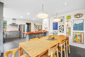 A modern kitchen with stainless steel appliances, a wooden dining table with chairs, and a wall decorated with various artworks. - The Hide at Big Hill (Big Hill)