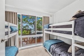A room with bunk beds, a sliding glass door, and a view of trees and a deck outside. - The Hide at Big Hill (Big Hill)