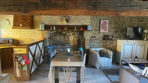 Una cocina rústica con un horno de piedra, vigas de madera, una mesa de comedor y un televisor.