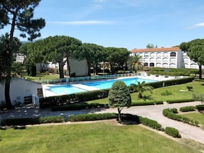 A swimming pool surrounded by well-maintained lawns and trees, with a building in the background. - Apartment with pool - 3 guests, 150m to beach (Argelès-sur-Mer)