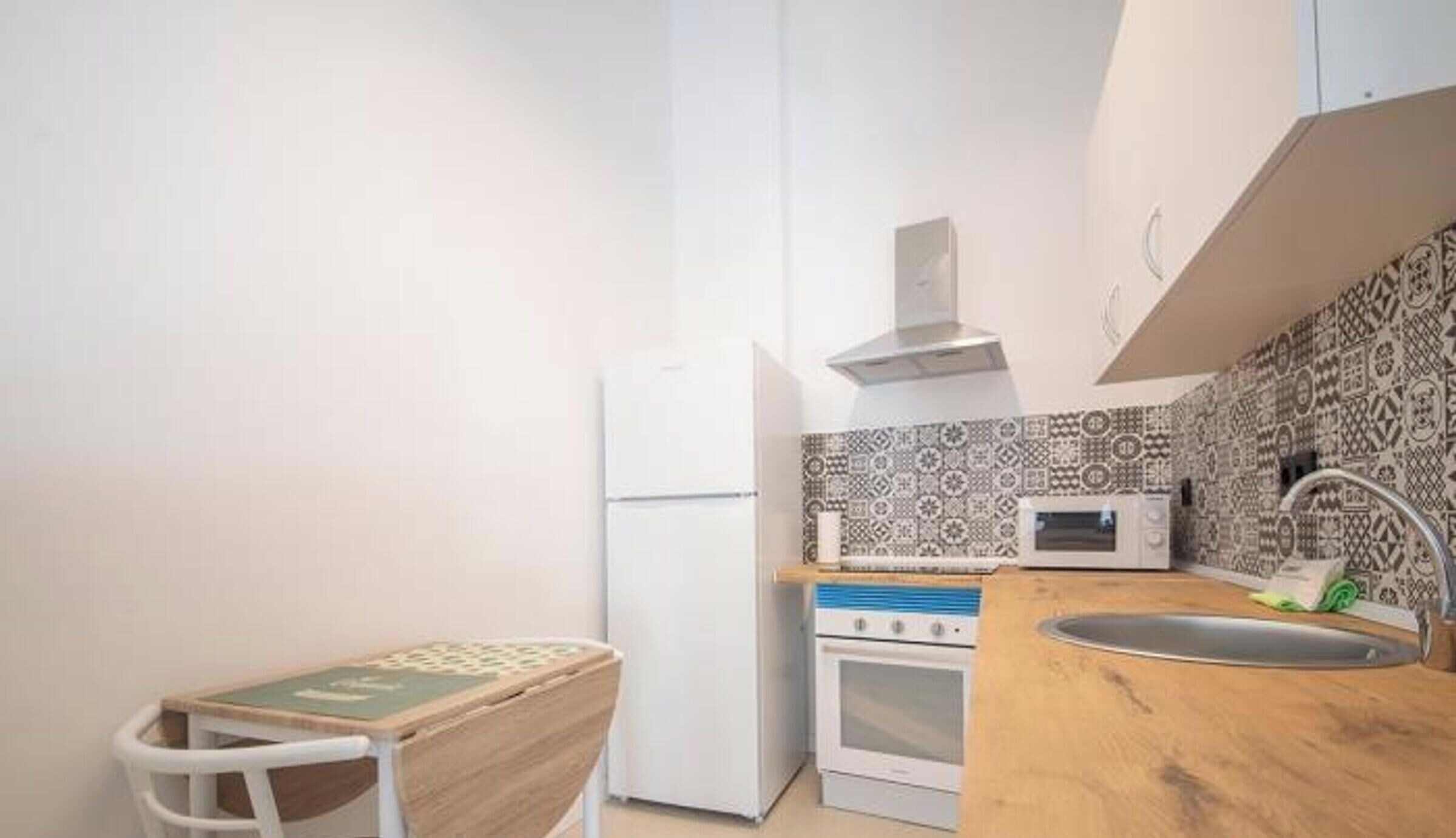 A compact kitchen with a refrigerator, microwave, oven, and a wooden countertop.