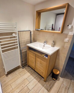 A bathroom with a white sink, wooden cabinets, a mirror, a towel rack, and a floor heater. - Le Perchoir Urbain, Duplex (Saint-Étienne)