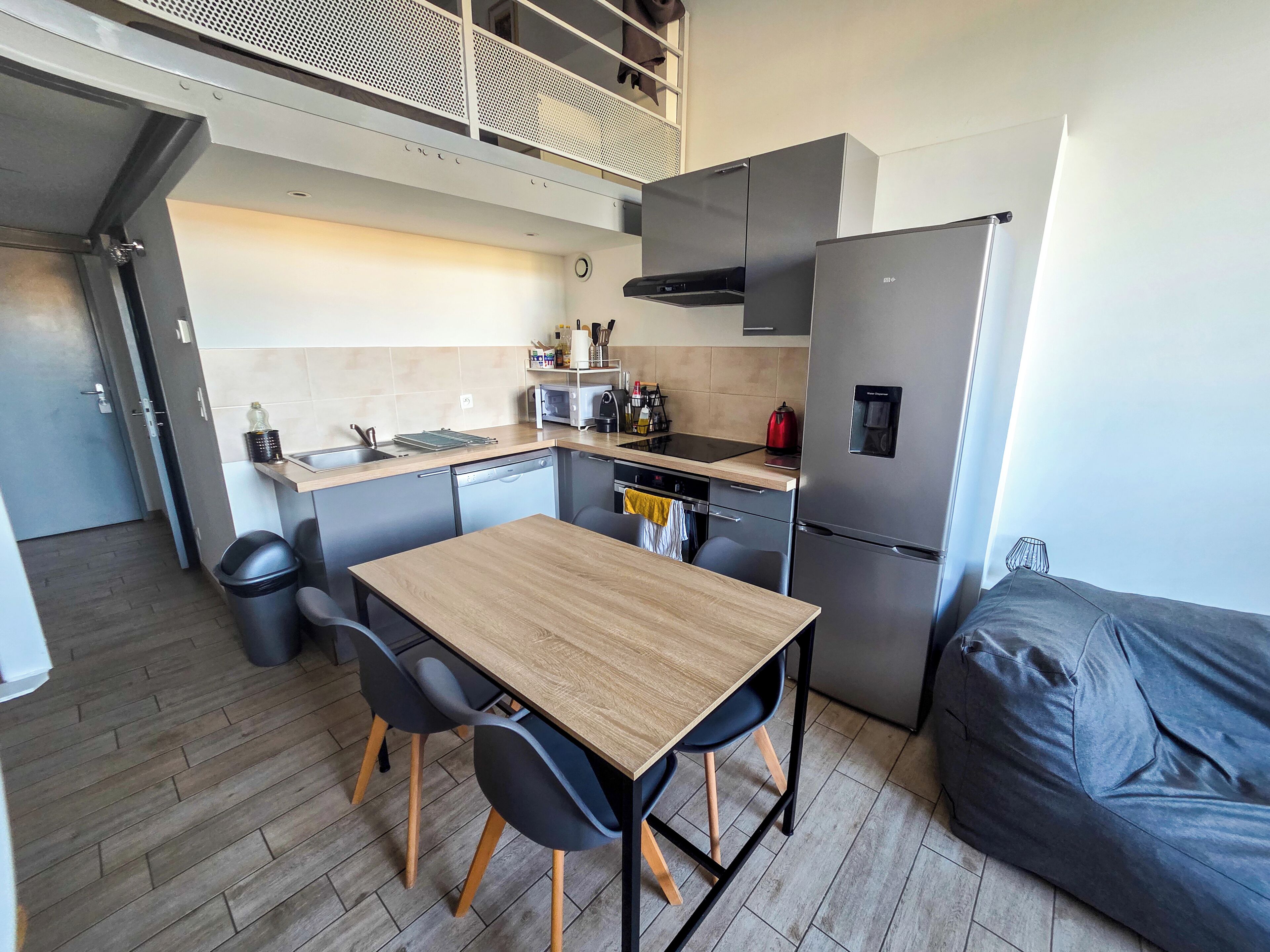 A compact kitchen with a dining table, chairs, a refrigerator, and a kettle.