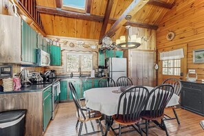 A wooden cabin interior with a kitchen, dining area, and a large window. - Charming Riverfront Home With Cozy Interiors, Dock, and Scenic Deck Views (Wiscasset)