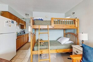 Una cama litera con escalera, un escritorio, una lámpara y una zona de cocina con armarios y un refrigerador.