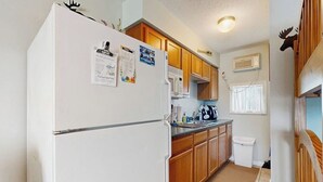 Una cocina compacta con armarios de madera, un refrigerador blanco, un microondas y un ventanal.