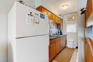 Una cocina compacta con armarios de madera, un refrigerador blanco, un microondas y un ventanal.