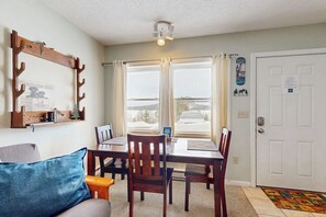 A dining area with a table, chairs, and a view through large windows. - Studio With Shared Dock & Amazing View of Moosehead Lake & Mt. Kineo (Rockwood)