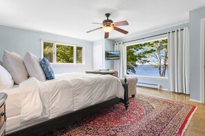 A bedroom with a bed, a ceiling fan, a TV, and a view of the outdoors. - Charming Home With Stunning bay Views, Sunroom, Gazebo, Deck, & Grill (Trenton)
