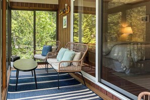 A room with wicker furniture, a bed, a table, and a large window with a view of greenery. - Heart Pond Hideaway (Orland)