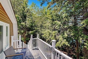 A wooden deck with white railings, surrounded by dense green trees. - Heart Pond Hideaway (Orland)