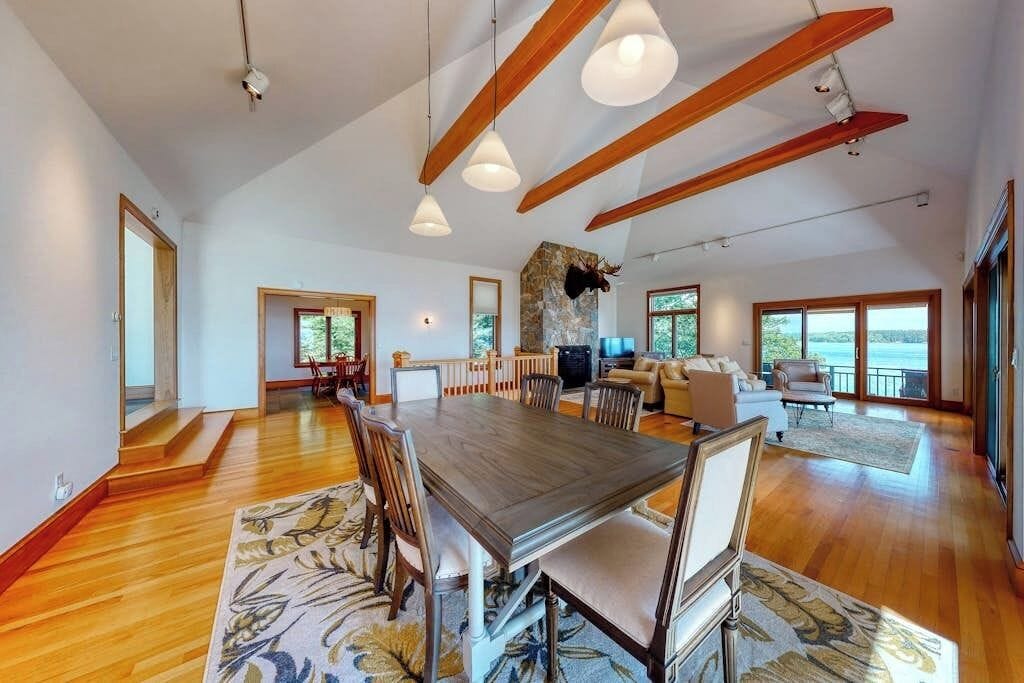 A spacious dining area with a wooden table and chairs, a stone accent wall, and large windows offering a view.