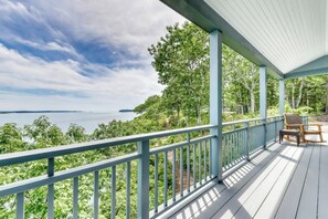 Eine überdachte Terrasse mit Geländer, mit Blick auf ein Gewässer und viel Grün.