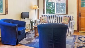 Et værelse med en sofa, to lænestole, et fjernsyn, en lampe og et vindue med en paraply.