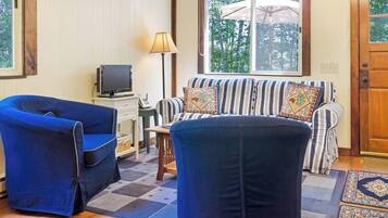 A room with a sofa, two armchairs, a television, a lamp, and a window with an umbrella.