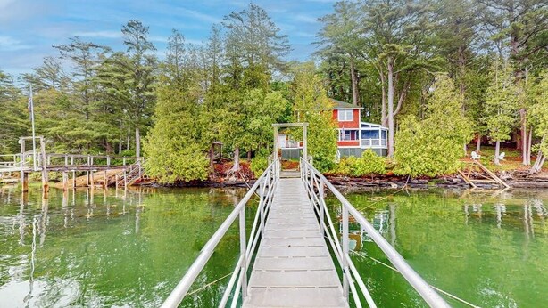 A wooden bridge leading to a house surrounded by trees and water. - Cozy, Waterfront Cabin-style Gem With Private Dock and Lovely Views (Bath)