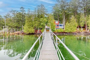 Eine Holzbrücke führt zu einem Haus, das von Bäumen und Wasser umgeben ist.
