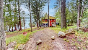 A red cabin with a porch, surrounded by trees and a lake. - Cozy, Waterfront Cabin-style Gem With Private Dock and Lovely Views (Bath)
