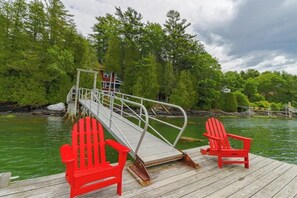 Eine Holzstege mit zwei roten Adirondack-Stühlen, einer Metallbrücke und einem Haus im Hintergrund.
