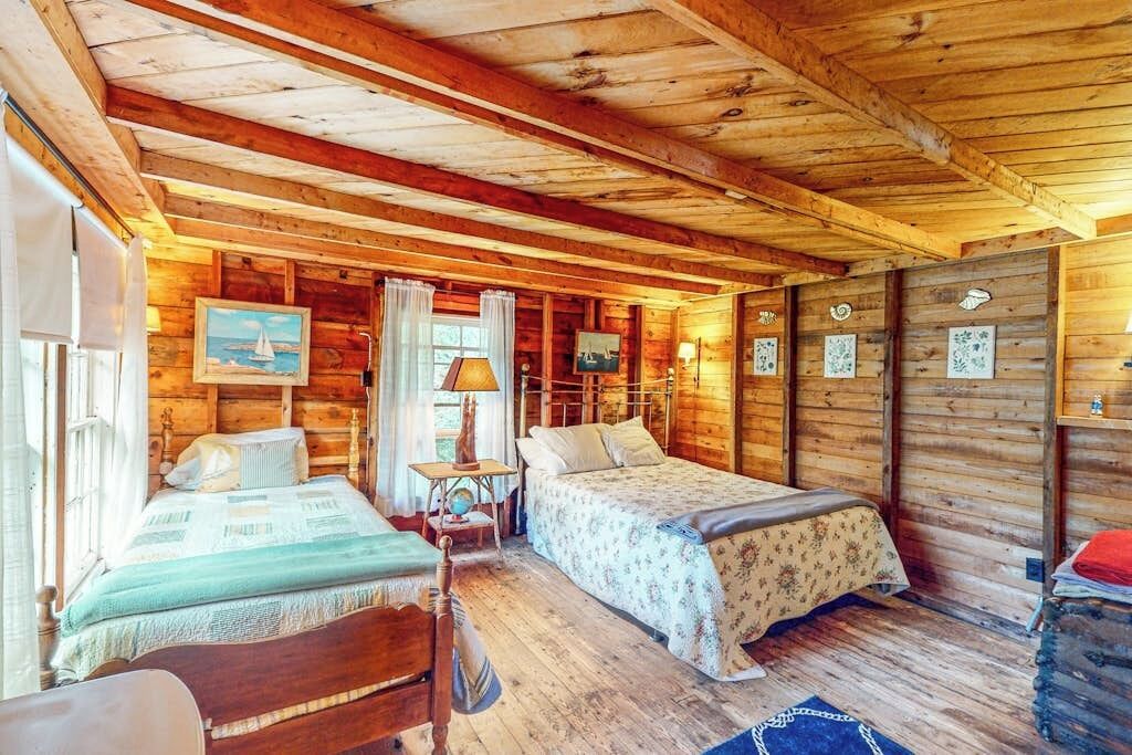 Una cabaña de madera con dos camas, una mesita y una ventana.