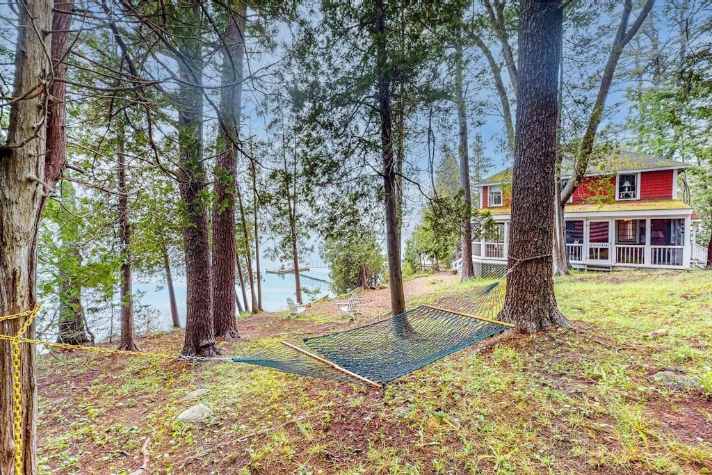 A hammock between trees near a house by a lake.