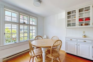 A dining area with a round table and four chairs, a window with multiple panes, and white cabinetry with glass doors. - Parker House: Historic Home - Walk Downtown, Dog-friendly & Washer/dryer (Camden)