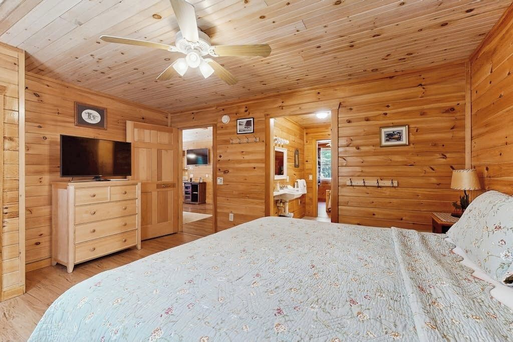Camera da letto in una baita di legno con un letto, una cassettiera, una televisione e una ventola a soffitto.