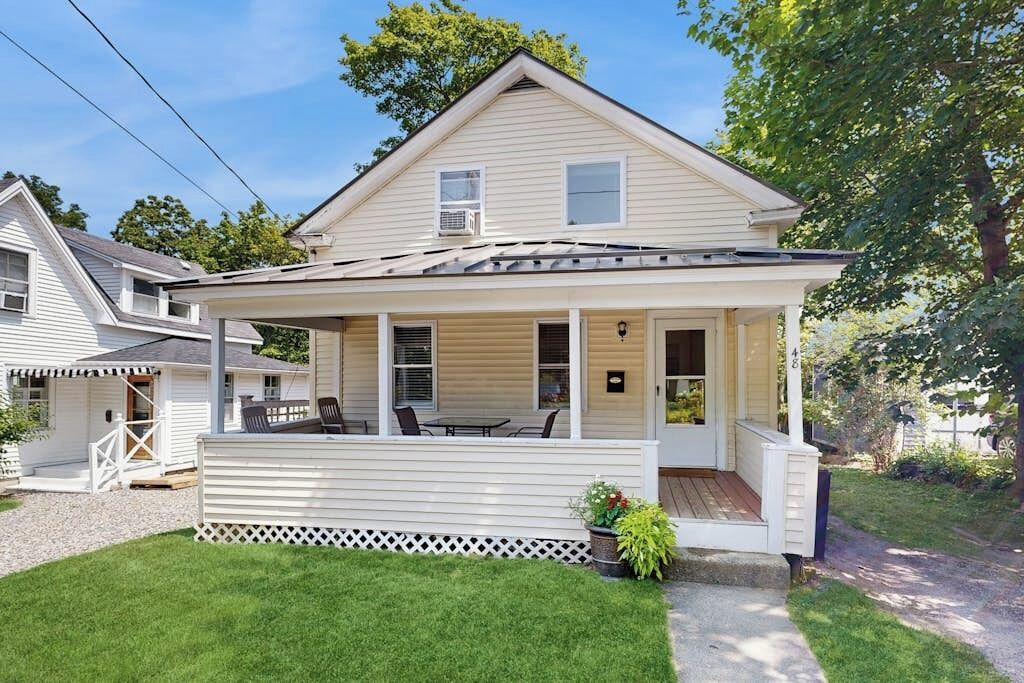 A two-story house with a covered porch, a small deck, and a well-maintained lawn.