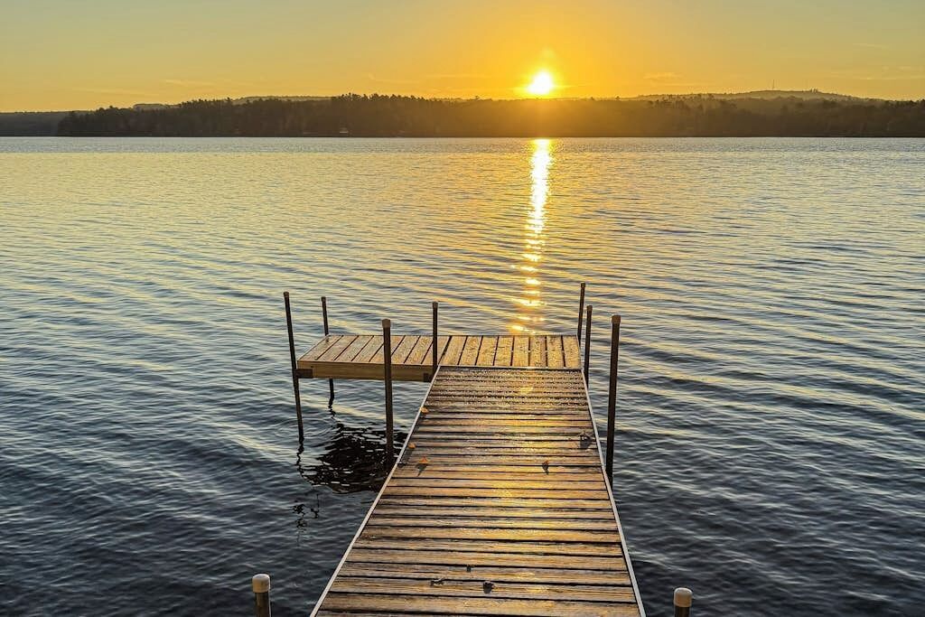 Un muelle de madera que se adentra en aguas tranquilas, con un atardecer al fondo.
