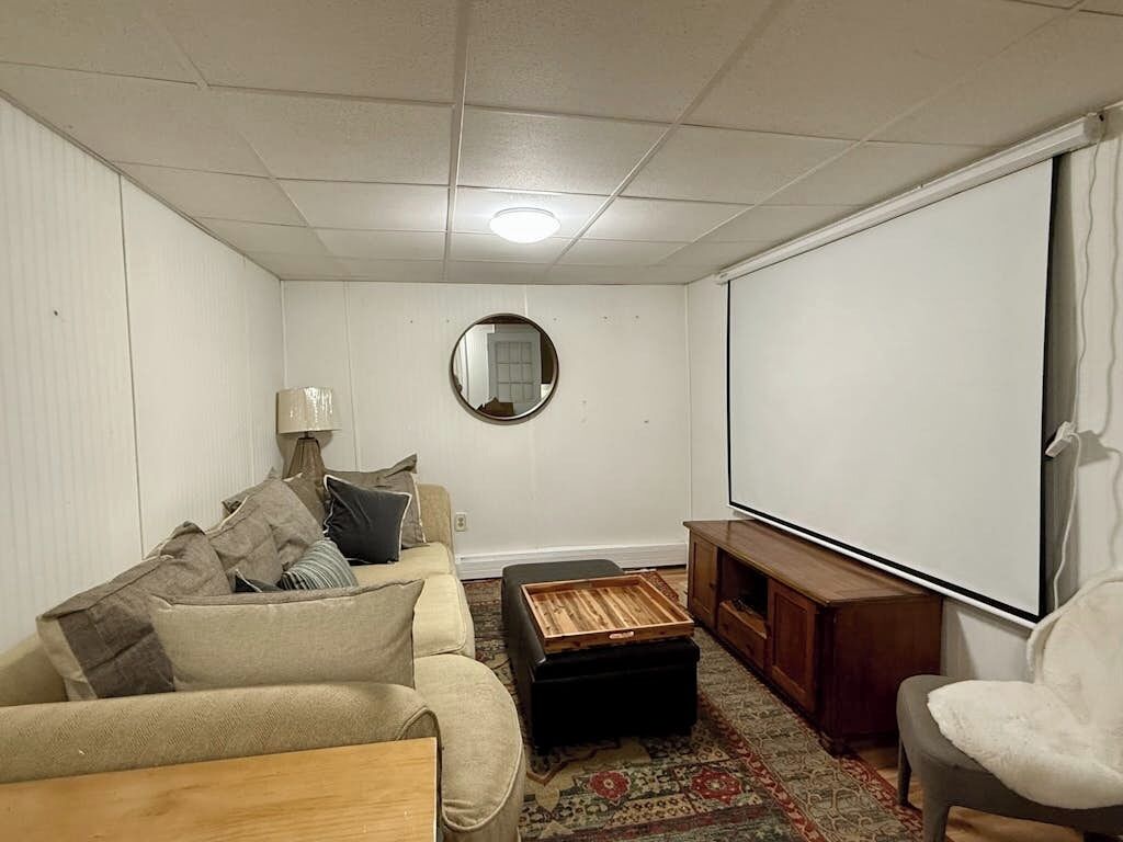 A living room with a sofa, ottoman, TV, and a mirror on the wall.