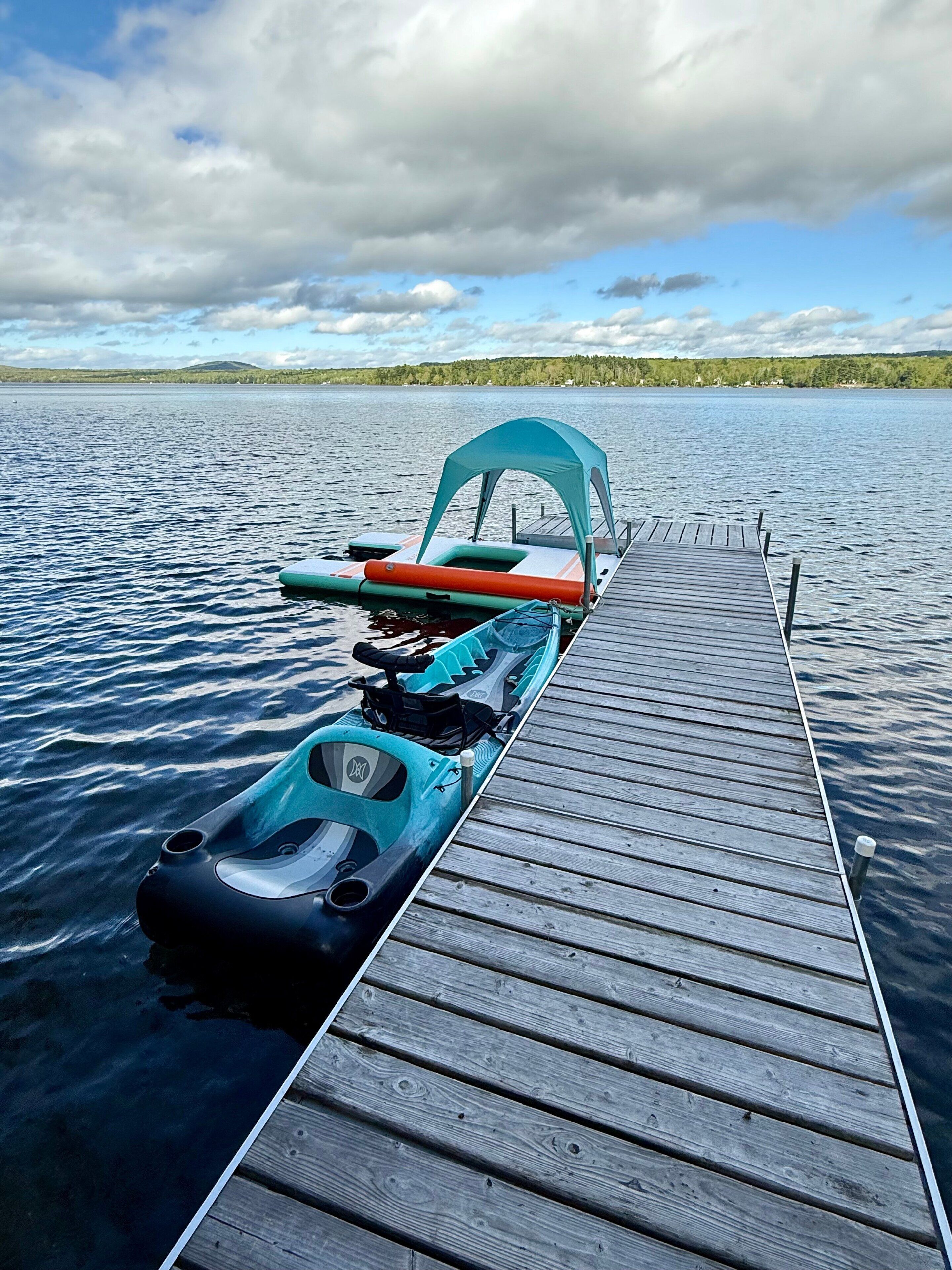 Un muelle de madera se adentra en un lago tranquilo, con kayaks y una canoa amarrados al final.