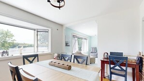 A dining area with a wooden table and chairs, a window with a view, and a ceiling light fixture. - Charming Lakefront House With Outdoor Firepit, Washer/dryer and Wifi (Gouldsboro)