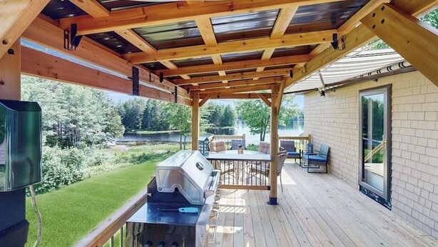 A covered outdoor deck with a grill, seating area, and a view of a lake. - Charming Lakefront House With Outdoor Firepit, Washer/dryer and Wifi (Gouldsboro)