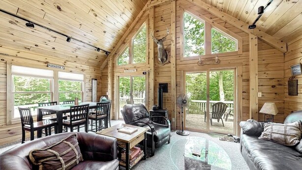 A wooden cabin interior with a dining area, leather furniture, and a large window. - Lakefront Cabin on First Roach Pond With Dock, Lake View & Firepit- Dog-friendly (Greenville)
