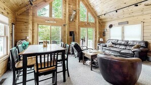 A log cabin interior with a dining table, chairs, a leather sofa, and a mounted deer head. - Lakefront Cabin on First Roach Pond With Dock, Lake View & Firepit- Dog-friendly (Greenville)