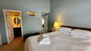 Ett hotellrum med en säng, ett nattduksbord med en lampa, ett badrum med en spegel och en väggdekoration.