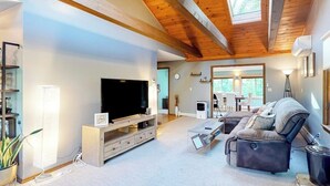 A modern living room with a large flat-screen TV, a sofa, a coffee table, and a wooden ceiling. - Tree-lined Home With Screened Porch & Perfect Midcoast Location (Damariscotta)