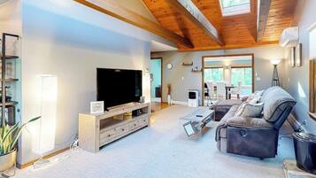 A modern living room with a large flat-screen TV, a sofa, a coffee table, and a wooden ceiling.