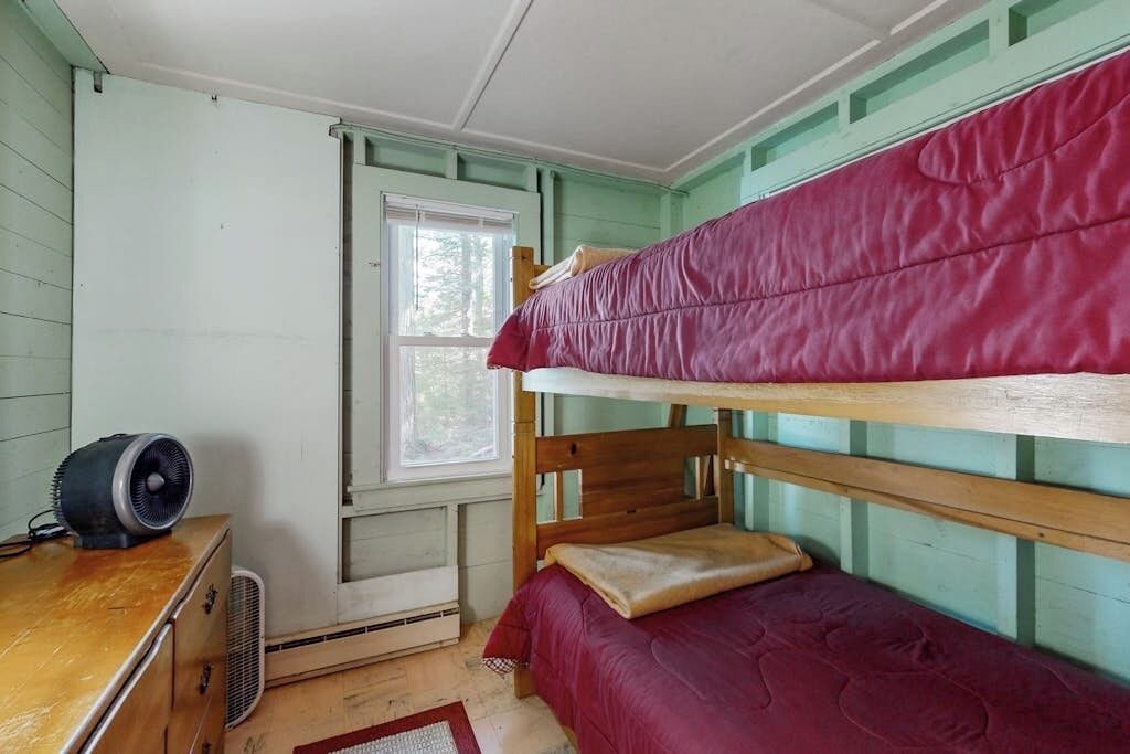 Een slaapkamer met stapelbed, raam, verwarming en een houten kledingkast.