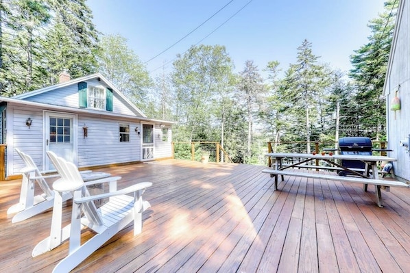 A wooden deck with Adirondack chairs, a grill, and a house with a gabled roof. - Sea View (Boothbay Harbor)