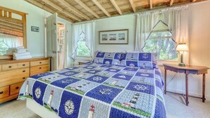 A bedroom with a wooden ceiling, a bed with a nautical-themed quilt, a dresser, a nightstand, and a window with curtains. - Sea View (Boothbay Harbor)