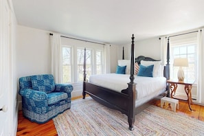 A bedroom with a four-poster bed, a blue patterned armchair, a small bedside table, and a window with curtains. - Historic Home w/ Gas Fireplace, Fast Wifi, & Private W/D - Snowbird-friendly (Warren)