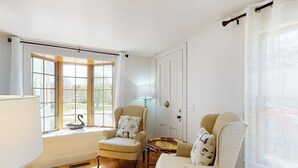 Um quarto com uma grande janela, duas poltronas, uma mesa pequena e um abajur.