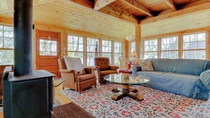 Ein gemütliches Blockhauskaminzimmer mit Kamin, Holzwänden, einer Couch und einem Glastisch.