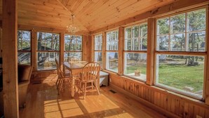 Ein Holzblockbau-Innenraum mit Esstisch, Stühlen, großen Fenstern und einer Chandelier.